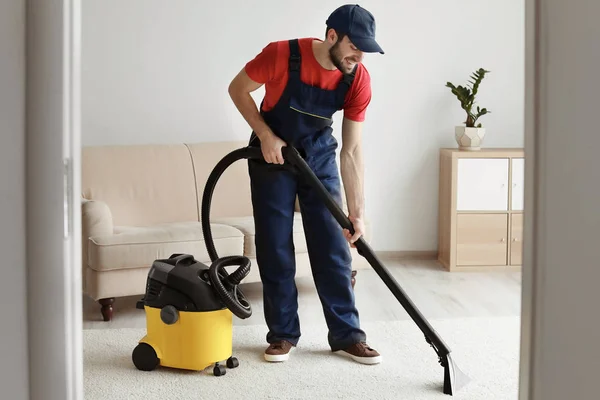 Pekerja laki-laki membersihkan karpet dengan vakum di ruang tamu — Stok Foto