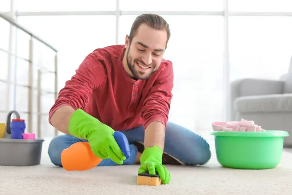 Молодой человек чистит ковер дома — стоковое фото