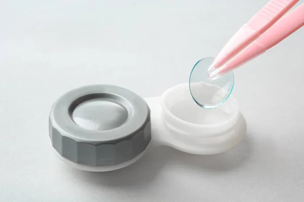 Pinças com lente de contato e recipiente em fundo claro, close-up — Fotografia de Stock