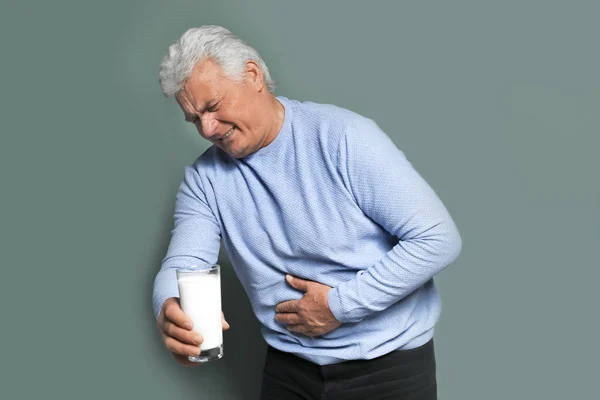 Mature man with dairy allergy holding glass of milk on color background — Stock Photo, Image