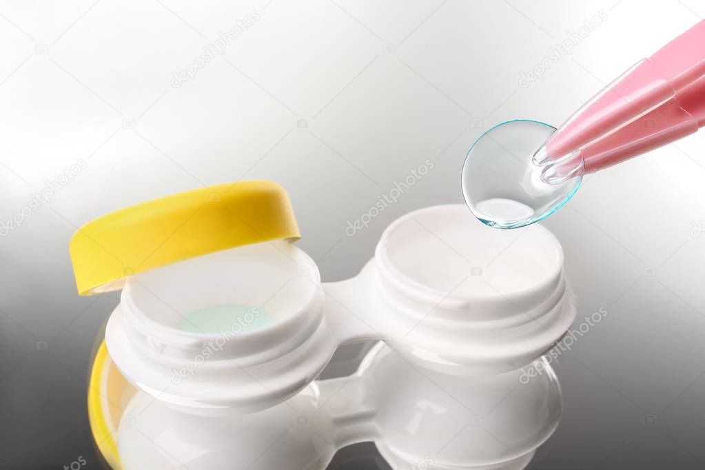 Taking contact lens from case on grey background, closeup