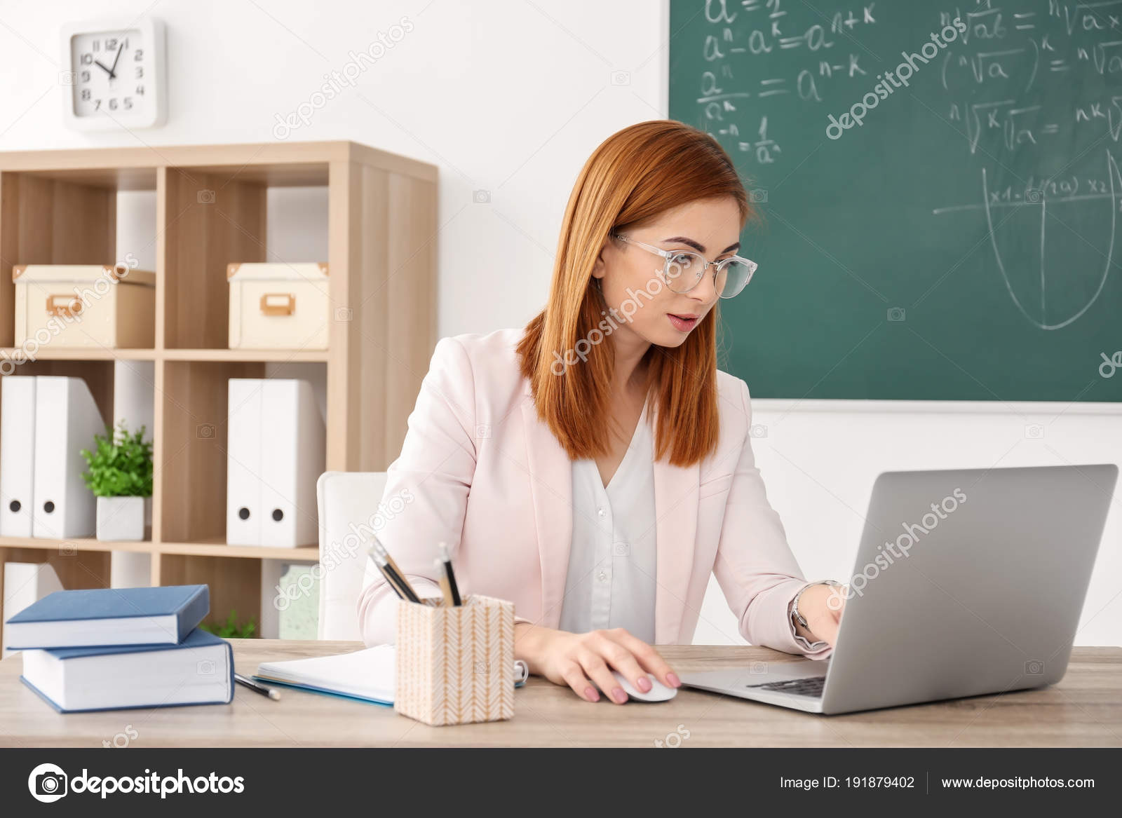 Beautiful young teacher with laptop sitting at table in classroom