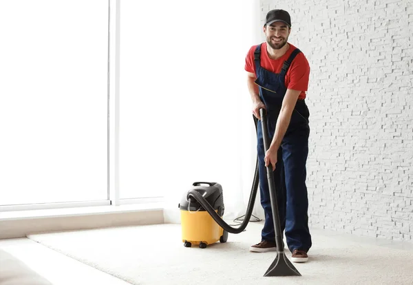 Trabalhador masculino tapete de limpeza com vácuo dentro de casa — Fotografia de Stock
