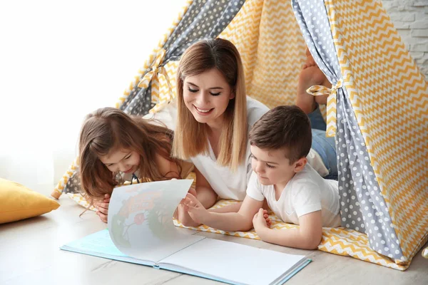 Nounou et petits enfants lisant le livre dans la tente à la maison — Photo