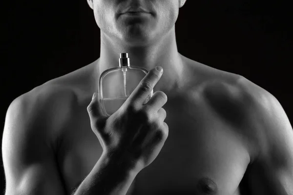 Handsome man using perfume on black background, closeup. Black and white effect