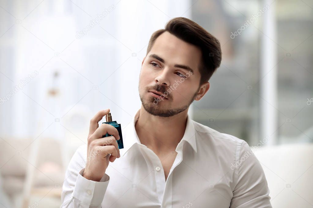 Handsome man in shirt using perfume on blurred background