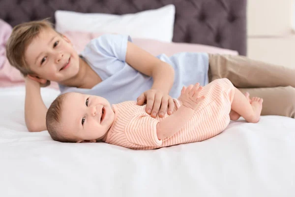 Schattige kleine baby met oudere broer liggend op bed thuis — Stockfoto