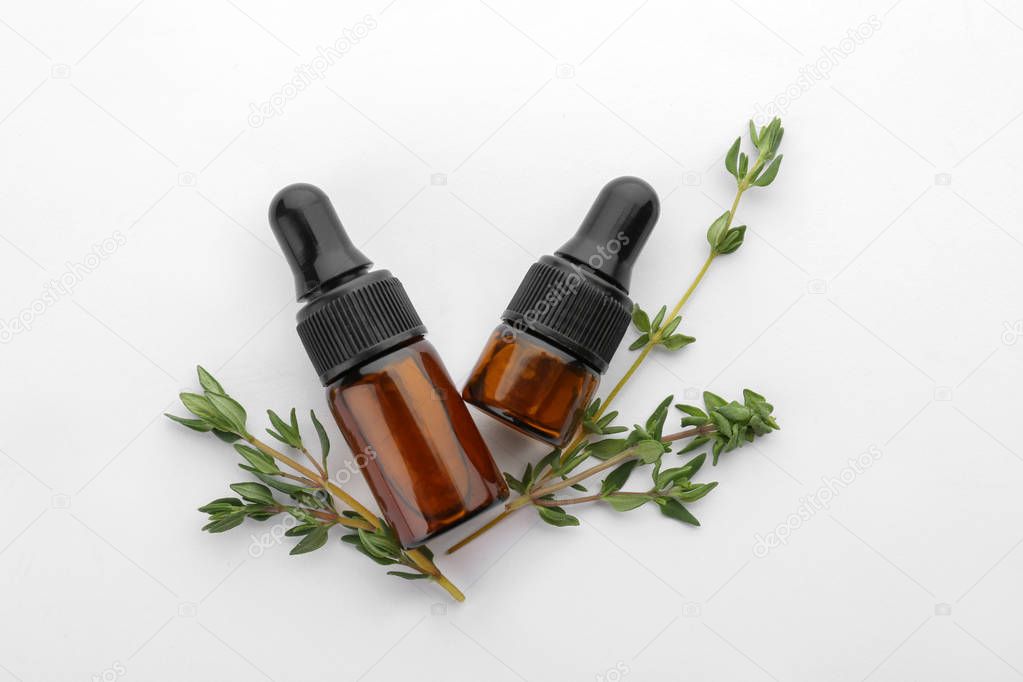 Bottles with thyme essential oil and fresh herb on white background