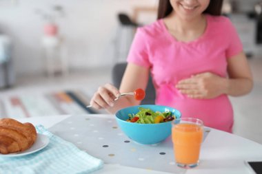 Genç hamile kadın mutfakta masada sebze salata yemek