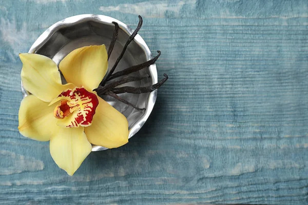 Bowl with vanilla flower and sticks on wooden background