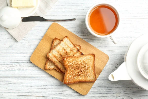 Board with toasted bread and cup of tea on wooden background, top view — Stock Photo, Image