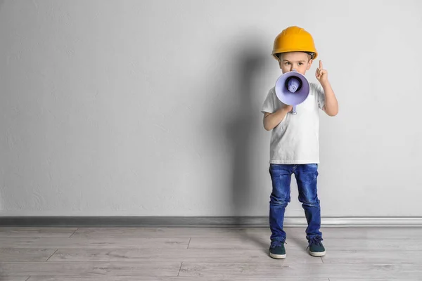 Чарівний маленький хлопчик в хардхаті з мегафоном біля світлої стіни — стокове фото