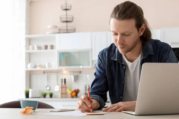 Молодой человек работает с ноутбуком на рабочем столе в домашнем офисе — стоковое фото