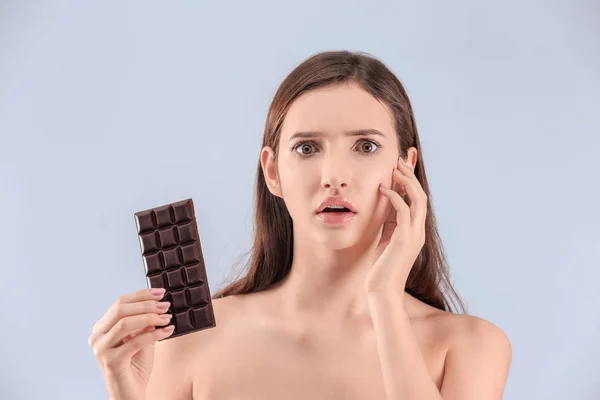 Chica adolescente con problemas de acné sosteniendo la barra de chocolate contra el fondo gris — Foto de Stock