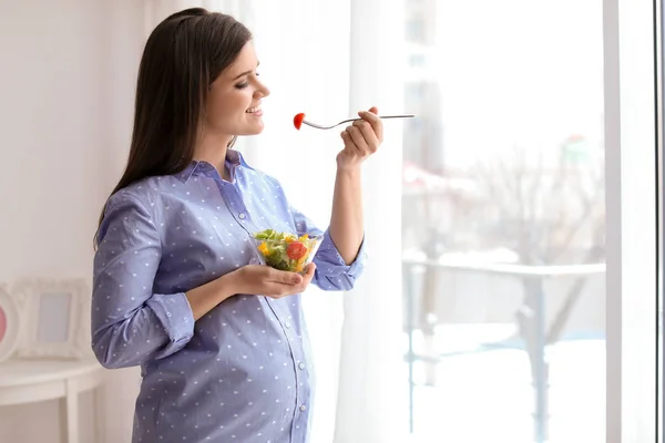 Mladá těhotná žena jíst zeleninový salát okna doma — Stock fotografie