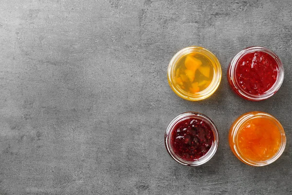 Gläser mit verschiedenen süßen Marmeladen auf grauem Hintergrund — Stockfoto