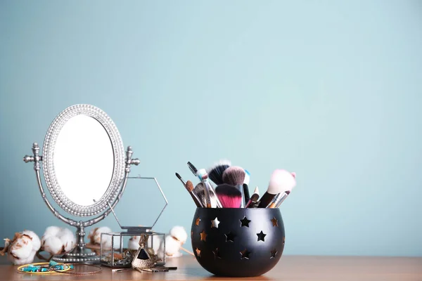 Soporte con cepillos de maquillaje profesional y espejo en la mesa cerca de la pared de color — Foto de Stock