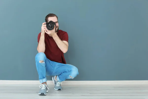Jovem fotógrafo com câmera profissional perto da parede de cor — Fotografia de Stock