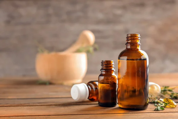 Bottles of essential oil with thyme on wooden table — Stock Photo, Image