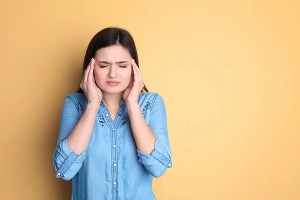 Jonge vrouw lijden aan hoofdpijn op kleur achtergrond — Stockfoto