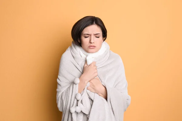 Jovem mulher envolto em cobertor sofrendo de frio no fundo de cor — Fotografia de Stock