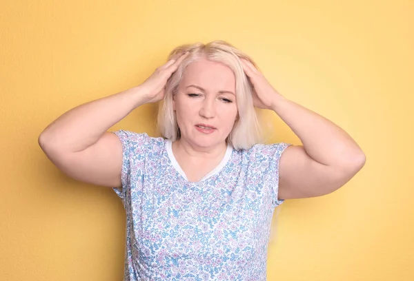 Mature woman suffering from headache on color background — Stock Photo, Image