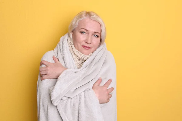 Femme mûre enveloppée dans une couverture souffrant de froid sur fond de couleur — Photo
