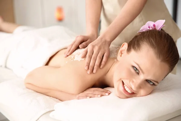 Hermosa mujer joven teniendo masaje con exfoliante corporal en el salón de spa —  Fotos de Stock
