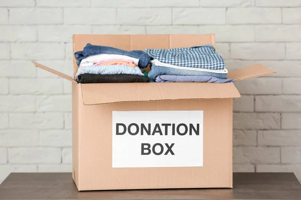 Donationen låda med kläder på bordet mot tegelvägg — Stockfoto