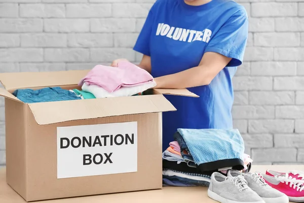 Mujer voluntaria recogiendo ropa y zapatos en la caja de donación en el interior — Foto de Stock
