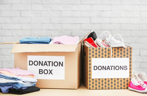 Cajas de donación con ropa y zapatos en la mesa contra la pared de ladrillo — Foto de Stock