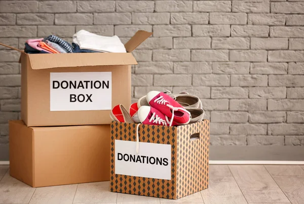 Donation boxes with clothes and shoes on floor against brick wall