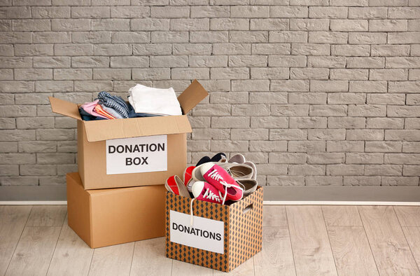 Donation boxes with clothes and shoes on floor against brick wall