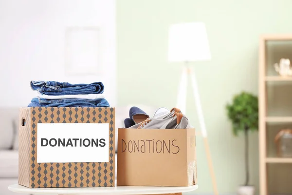 Spendenboxen mit Kleidung und Schuhen auf Tisch drinnen — Stockfoto