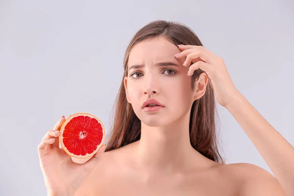 Teenage girl with acne problem holding grapefruit against grey background — Stock Photo, Image