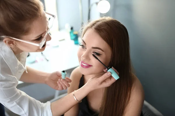 Artista de maquiagem profissional trabalhando com bela jovem no estúdio — Fotografia de Stock