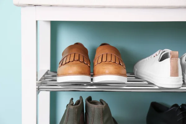 Коллекция стильной обуви на стойке хранения возле цветной стены — стоковое фото