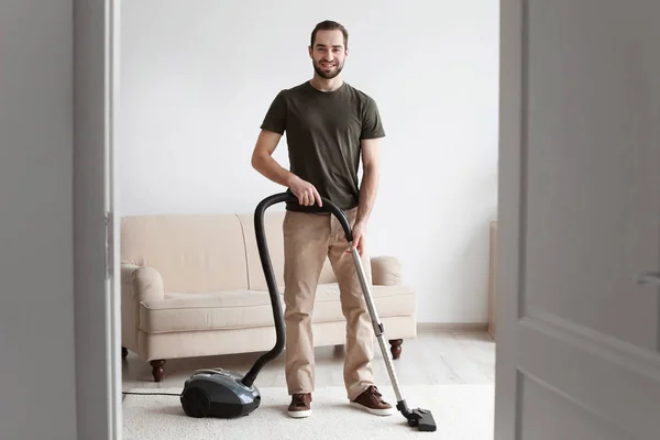 Молодий чоловік прибирає килим з вакуумом у вітальні — стокове фото