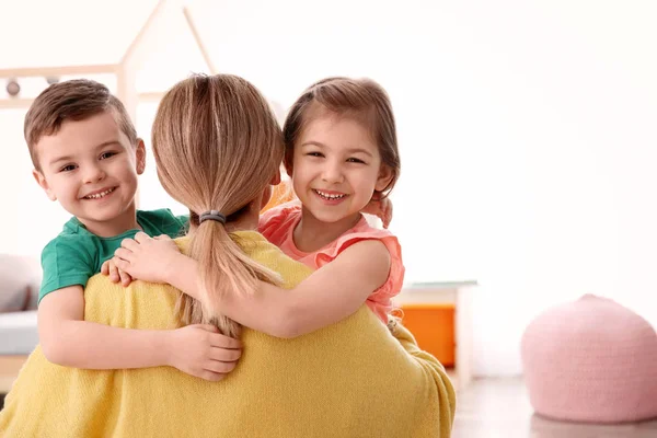 Niedliche kleine Kinder umarmen ihr Kindermädchen zu Hause — Stockfoto