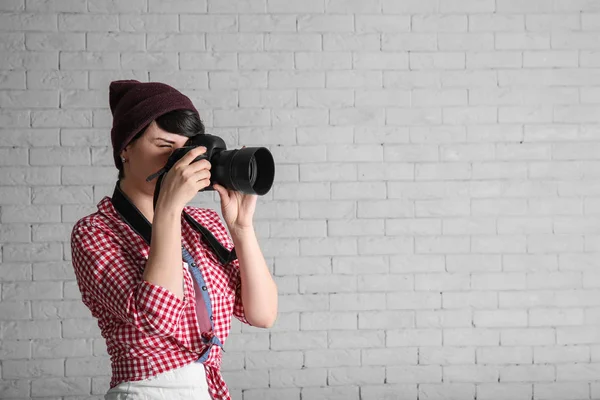 Jonge vrouwelijke fotograaf met de camera op baksteen achtergrond — Stockfoto