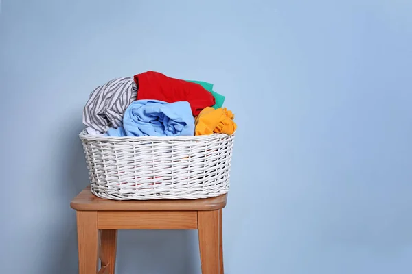 Laundry basket with dirty clothes on stool against color background — Stock Photo, Image