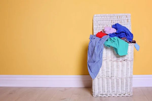 Корзина для белья с грязной одеждой на полу возле цветной стены — стоковое фото