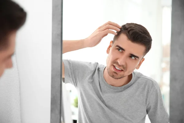 Junger Mann mit Haarausfall schaut in Spiegel im Haus — Stockfoto