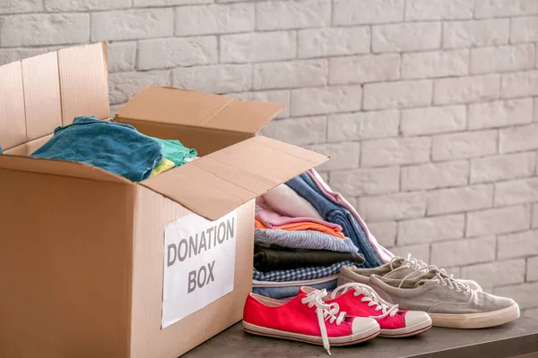 Donation box with clothes and shoes on table against brick wall