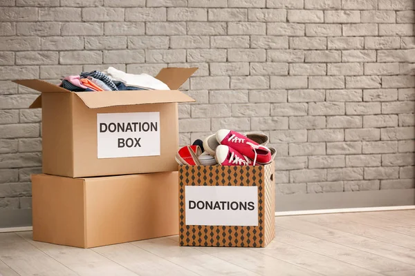 Cajas de donación con ropa y zapatos en el suelo contra la pared de ladrillo — Foto de Stock