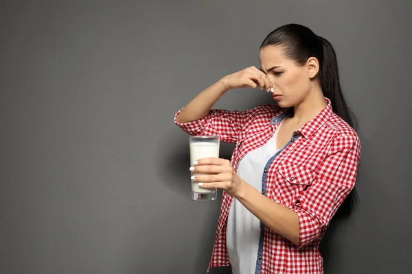 Молодая женщина с аллергией на молоко держит стакан молока на сером фоне — стоковое фото