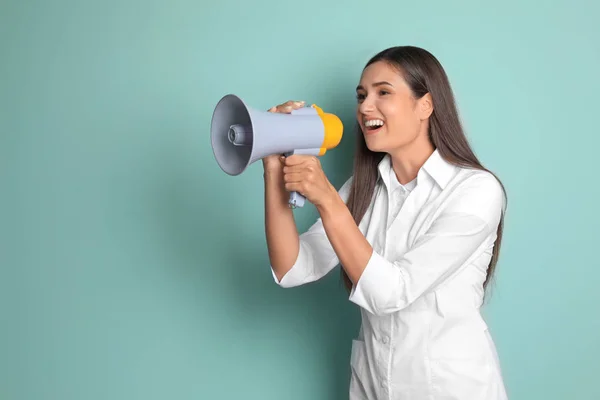 Doctora joven usando megáfono sobre fondo de color — Foto de Stock