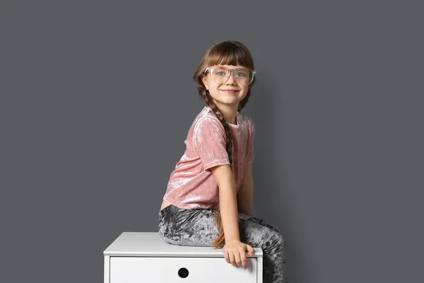 Petite fille mignonne assise sur la commode unité près du mur gris — Photo