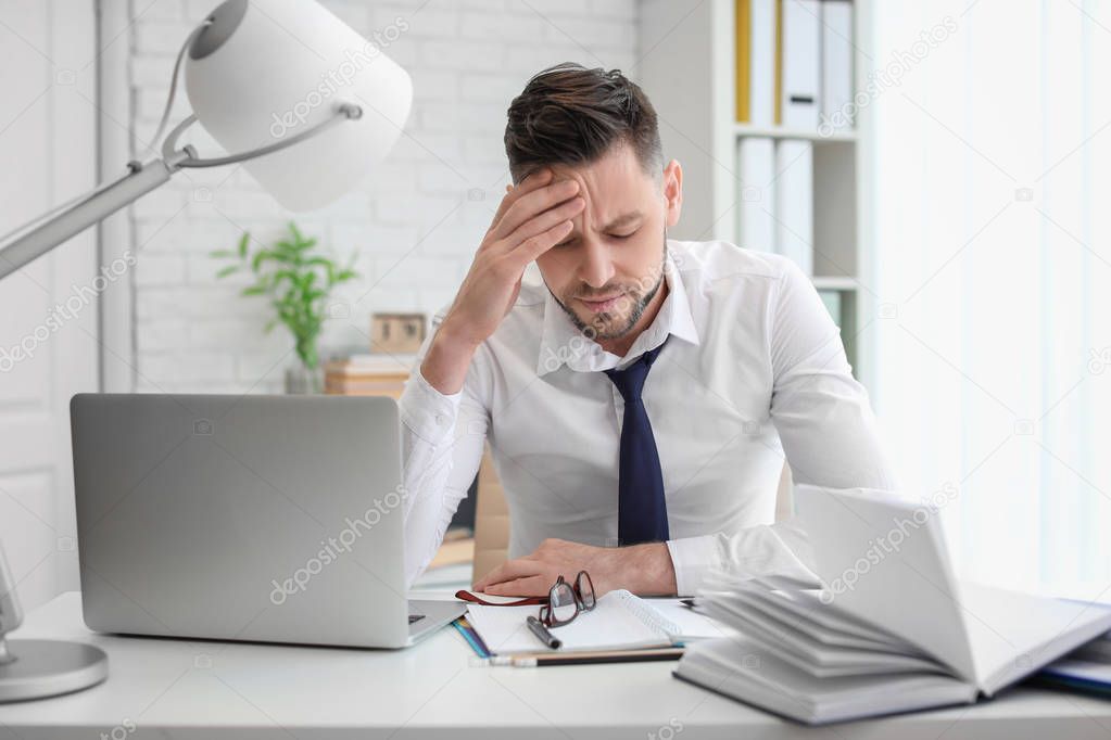 Man suffering from headache while sitting at table in office