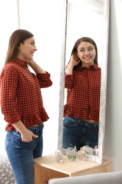 Jovem bela mulher olhando no espelho dentro de casa — Fotografia de Stock